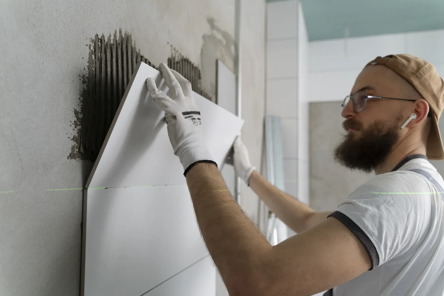 Tile installer pressing a large white wall tile onto freshly combed adhesive during a bathroom renovation