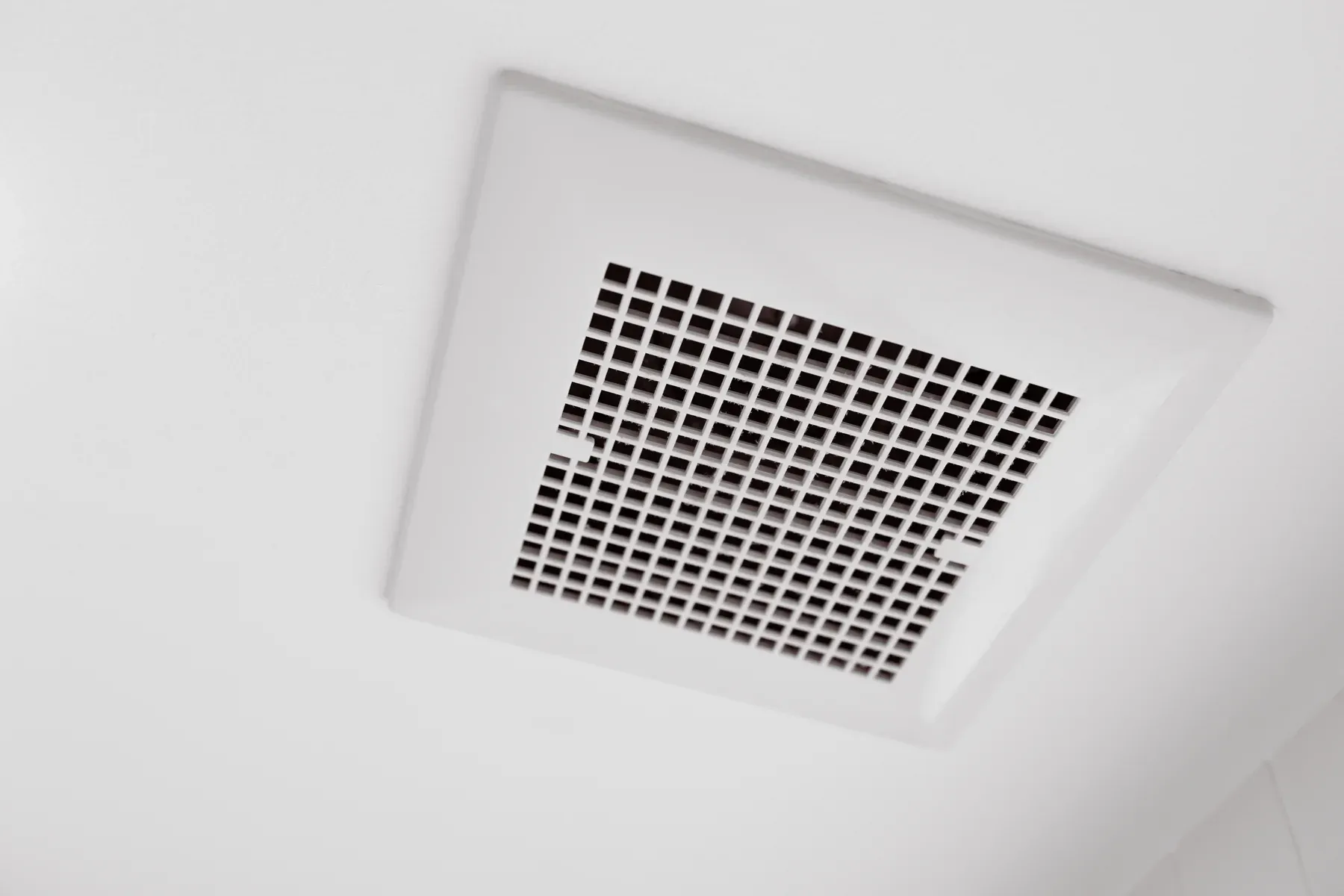 White square exhaust fan grille set into a smooth bathroom ceiling