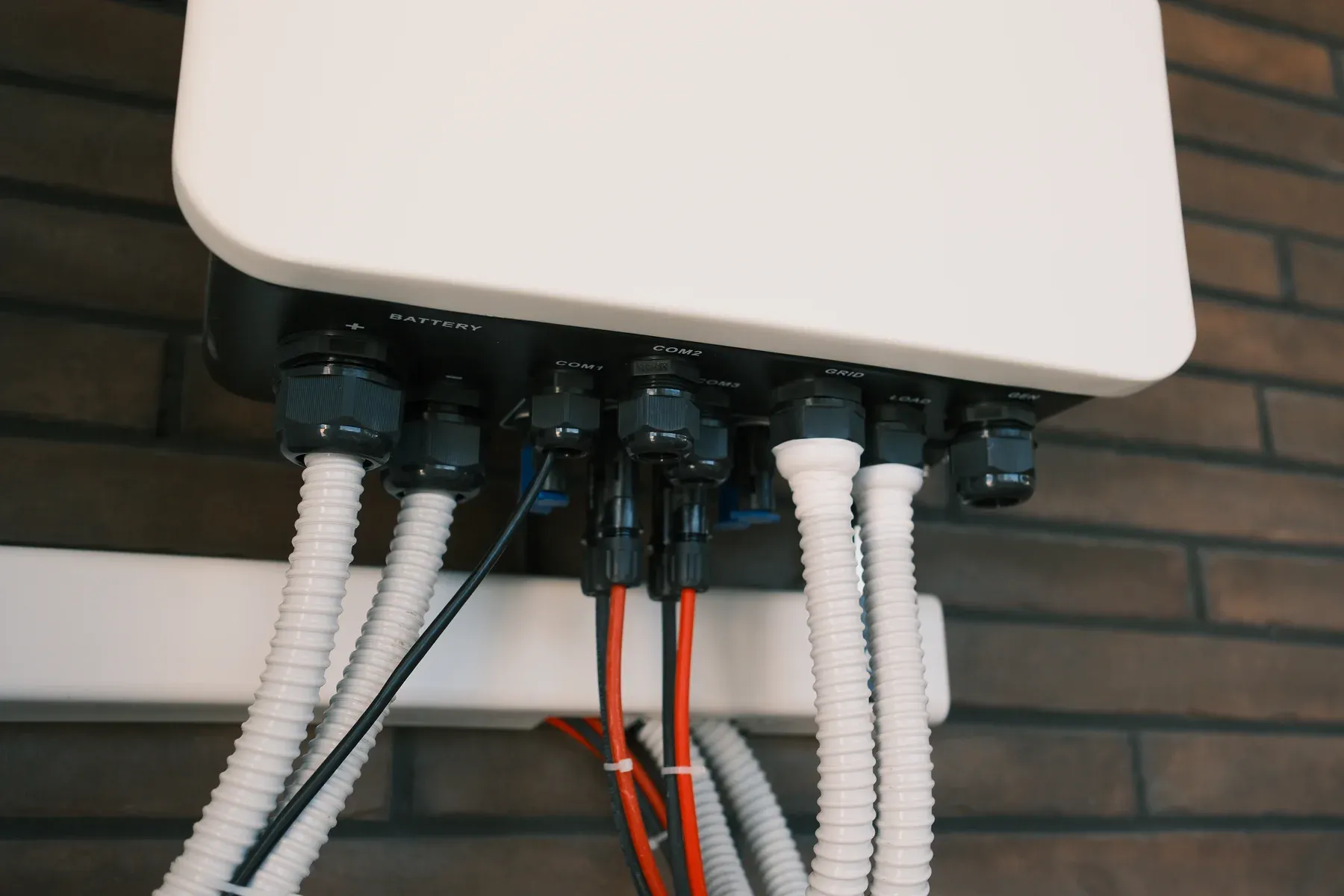 Underside of a wall-mounted hybrid inverter with battery, grid and load cables in conduit
