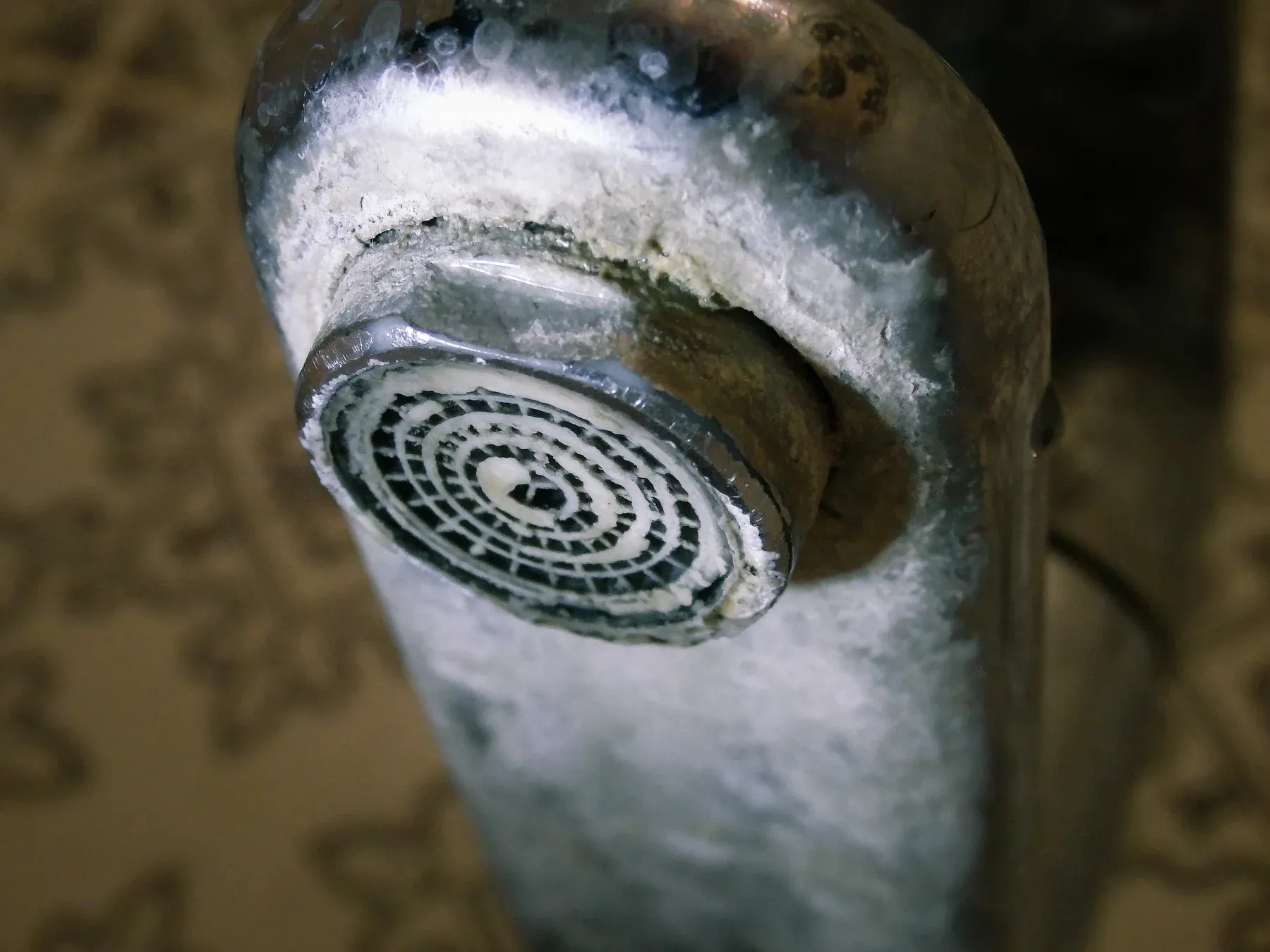 Close-up of a chrome bathroom faucet and aerator crusted with white limescale deposits
