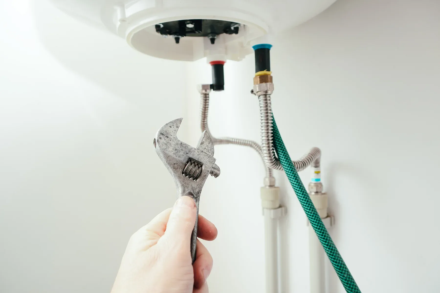 Plumber holding a wrench beneath a white storage water heater with a green drain hose attached