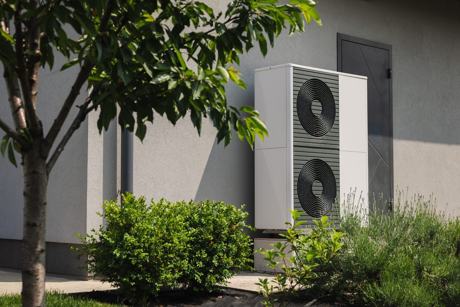 Modern outdoor heat pump unit installed beside a home, surrounded by shrubs