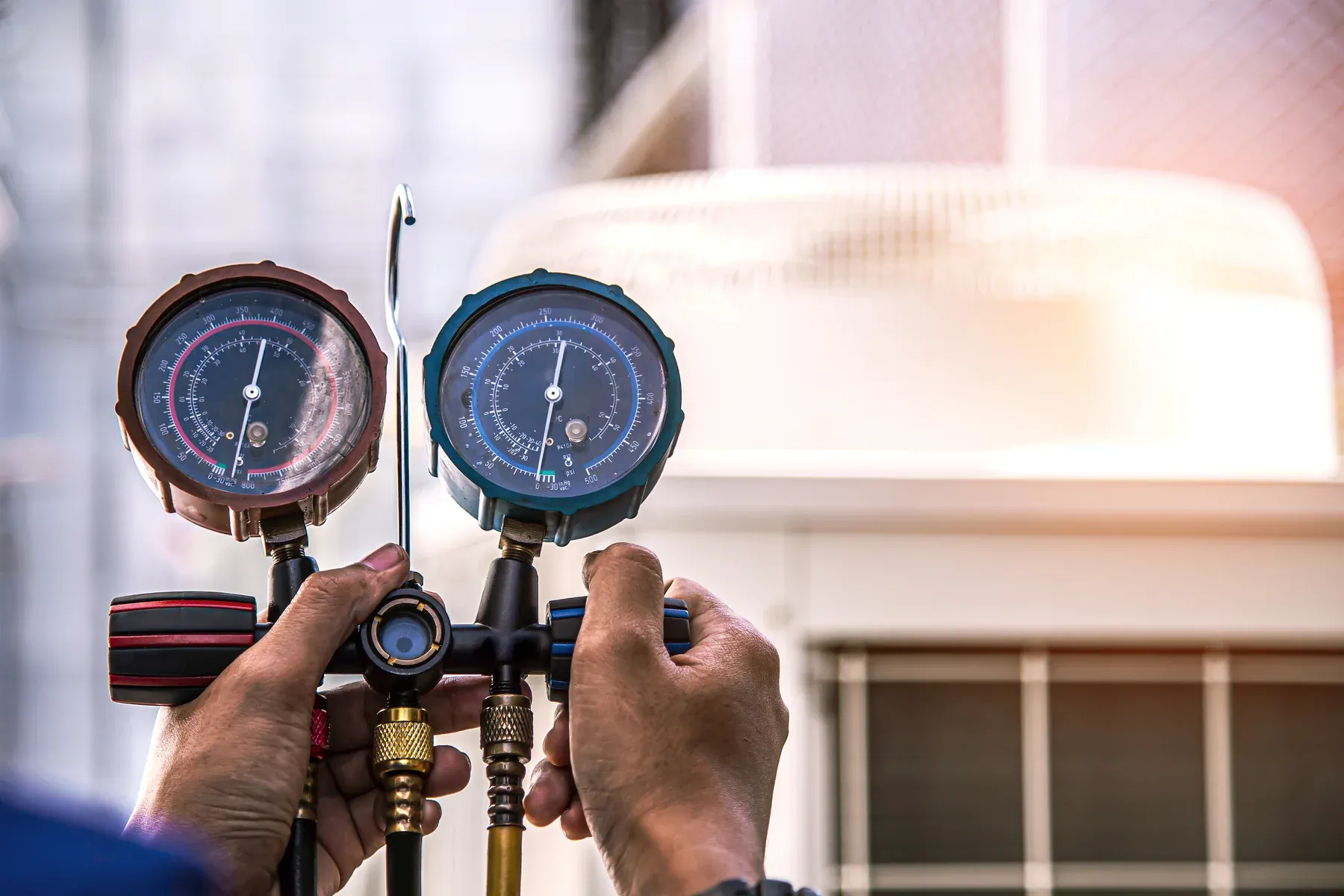 Technician holding a refrigerant manifold gauge set in front of an outdoor air conditioner