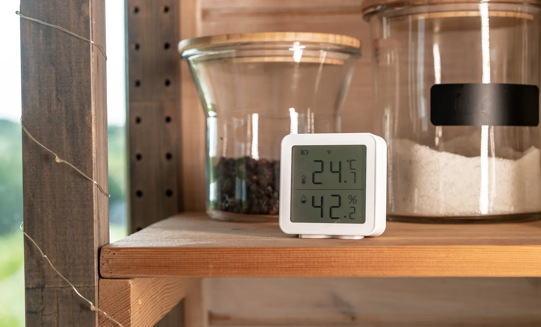 Small digital monitor on a wooden shelf showing indoor temperature and 42 percent humidity