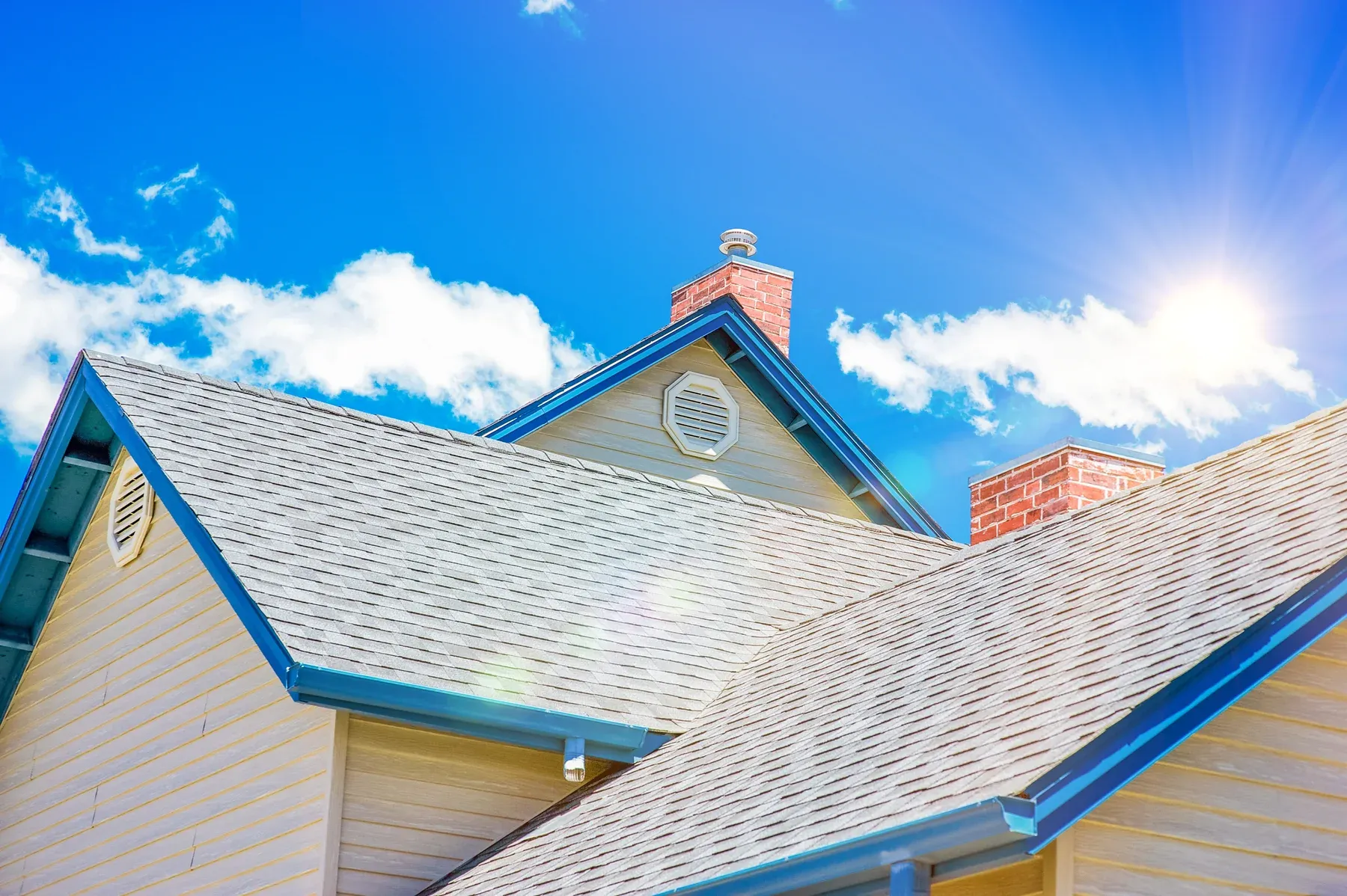 Light gray shingle roof of a two-story house under bright midday sun and blue sky