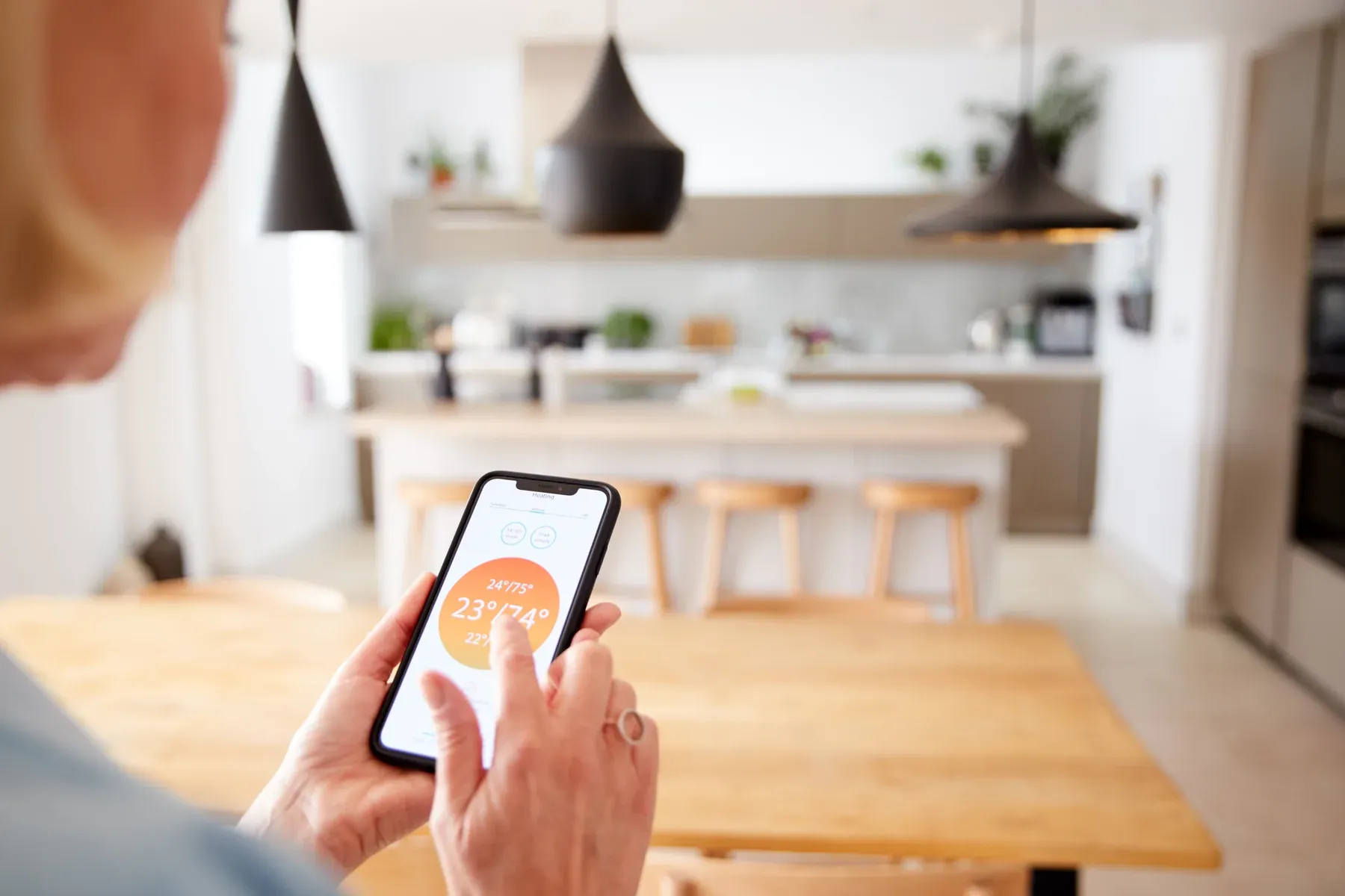 Hands holding a smartphone showing a temperature control app above a kitchen table